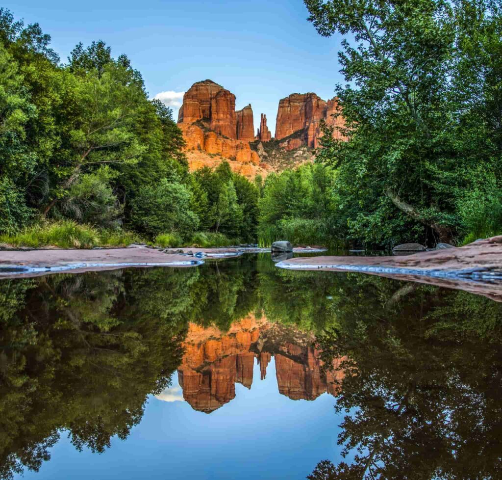 Cathedral Rock spires glowing orange at sunset and mirrored in a calm pool of water