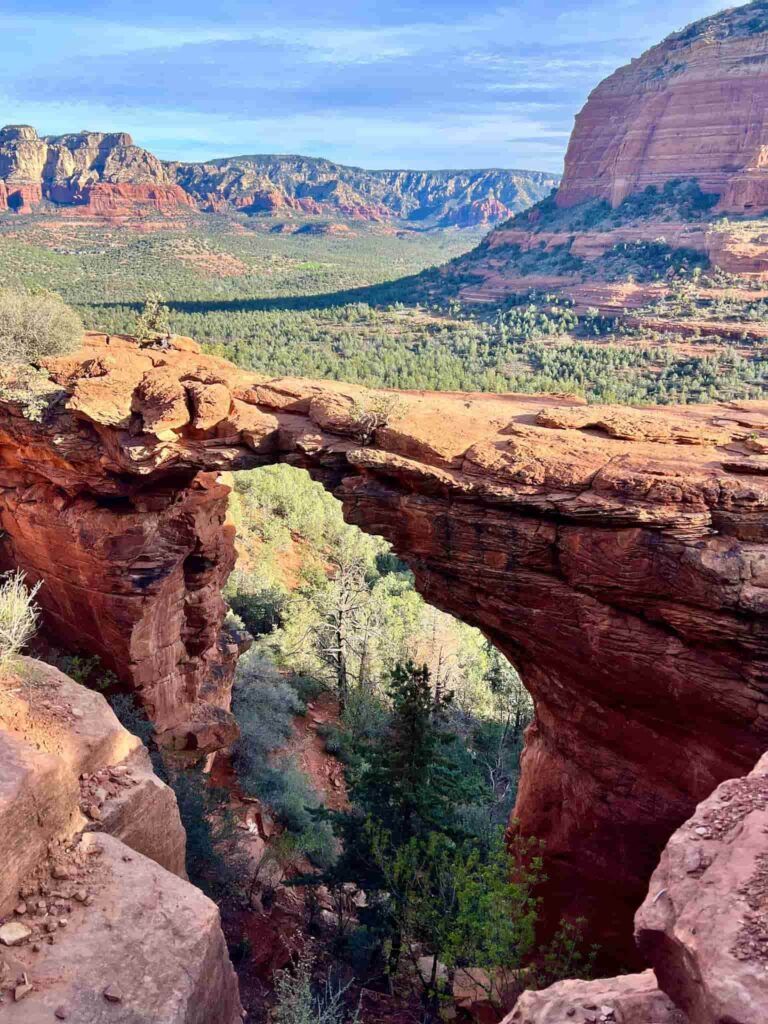 Natural sandstone span of Devils Bridge overlooking forested valleys and distant red-rock cliffs